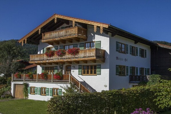 Ein zweistöckiges Gebäude mit Balkonen, Holellläufchen und grünen Fensterläden.