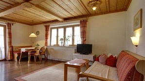 A cozy living room with a wooden ceiling, a sofa, a television, and a dining area with a table and chairs. - Farmhouse with 1 bedroom (Inzell, Deutschland)