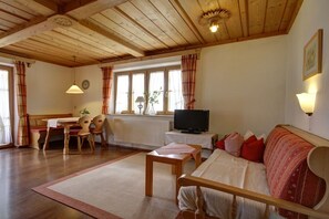 Ein gemütliches Wohnzimmer mit Holzboden, einer Couch, einem Fernseher und einem Essbereich mit Tisch und Stühlen.