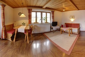 A cozy room with a wooden ceiling, a dining table with chairs, a sofa, a TV, and a window with curtains.