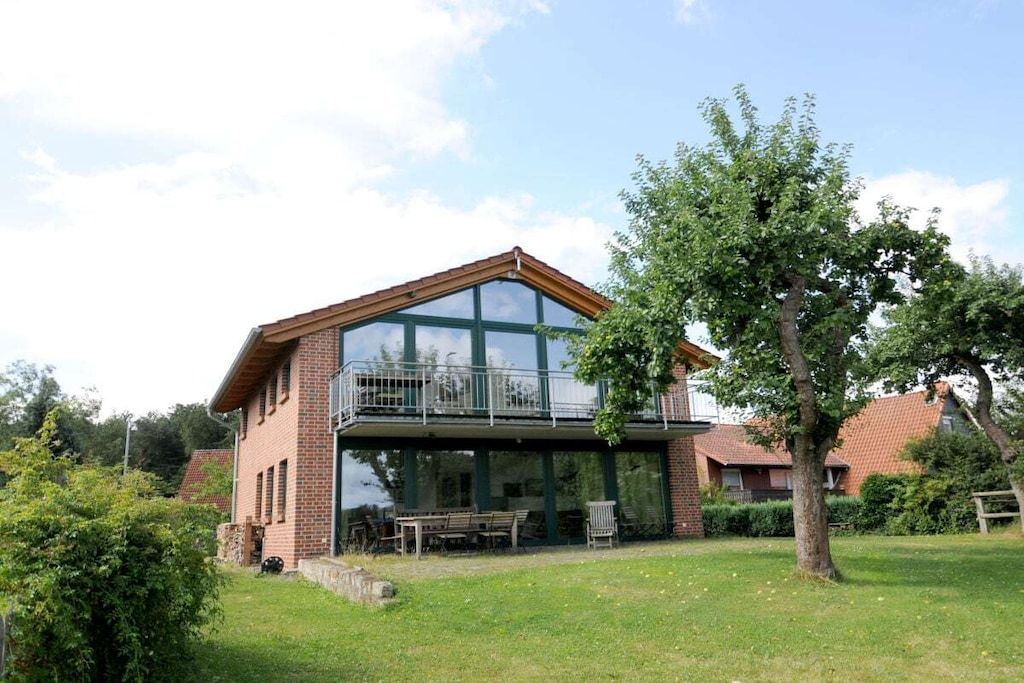 Ein zweistöckiges Haus mit Balkon, Rasen und Baum.