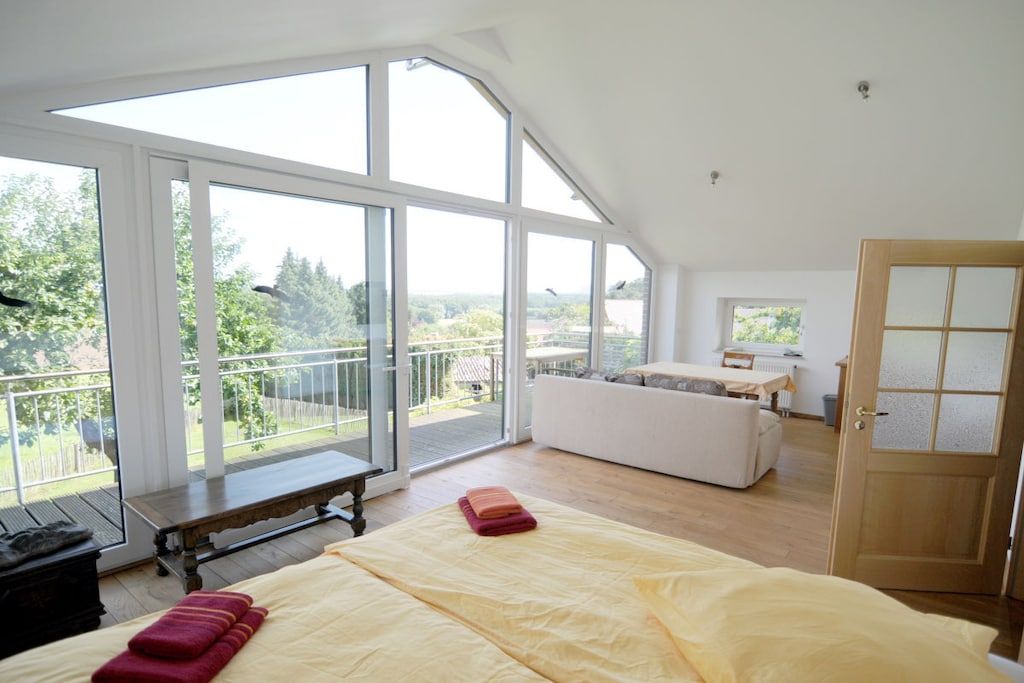 A bedroom with a large window, a bed, a bench, and a white sofa.