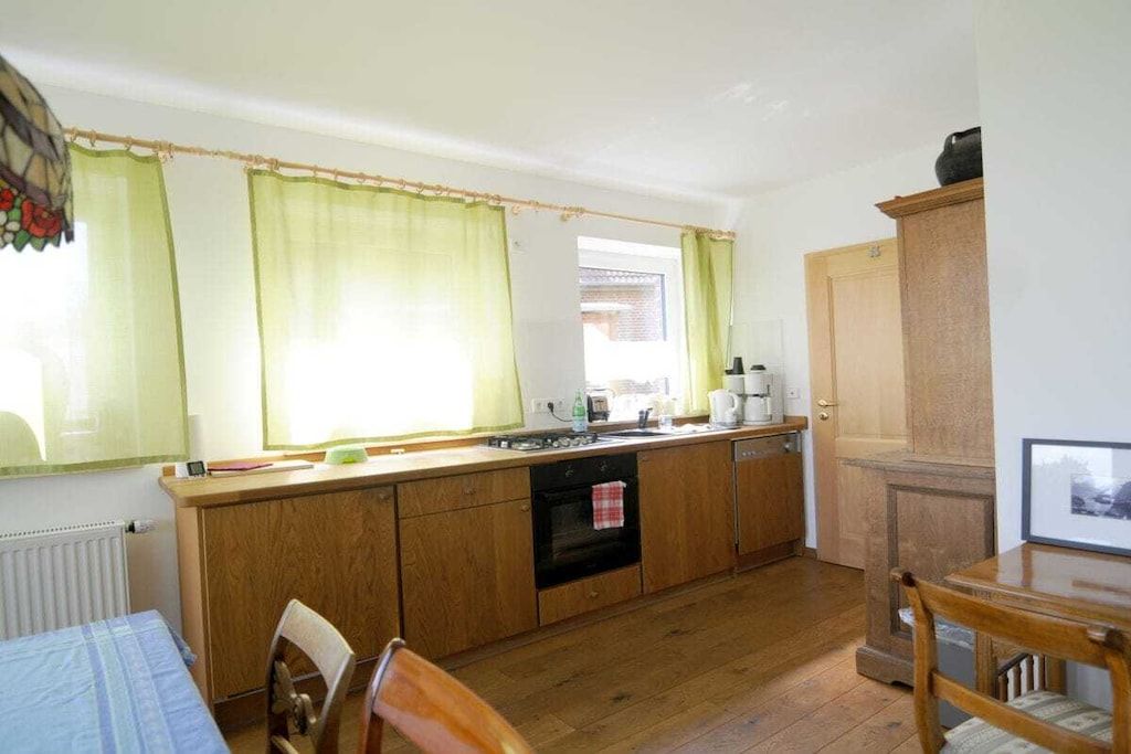 A compact kitchen with wooden cabinets, a built-in oven, and a window with curtains.