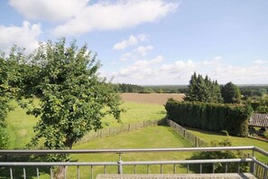 Blick von einem Balkon auf ein Wiesenfeld, einen Baum und einen Holzzaun.
