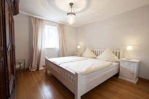 Ein Schlafzimmer mit einem Doppelbett, Nachttischen, einem Schranken und einem Vorhangfenster.