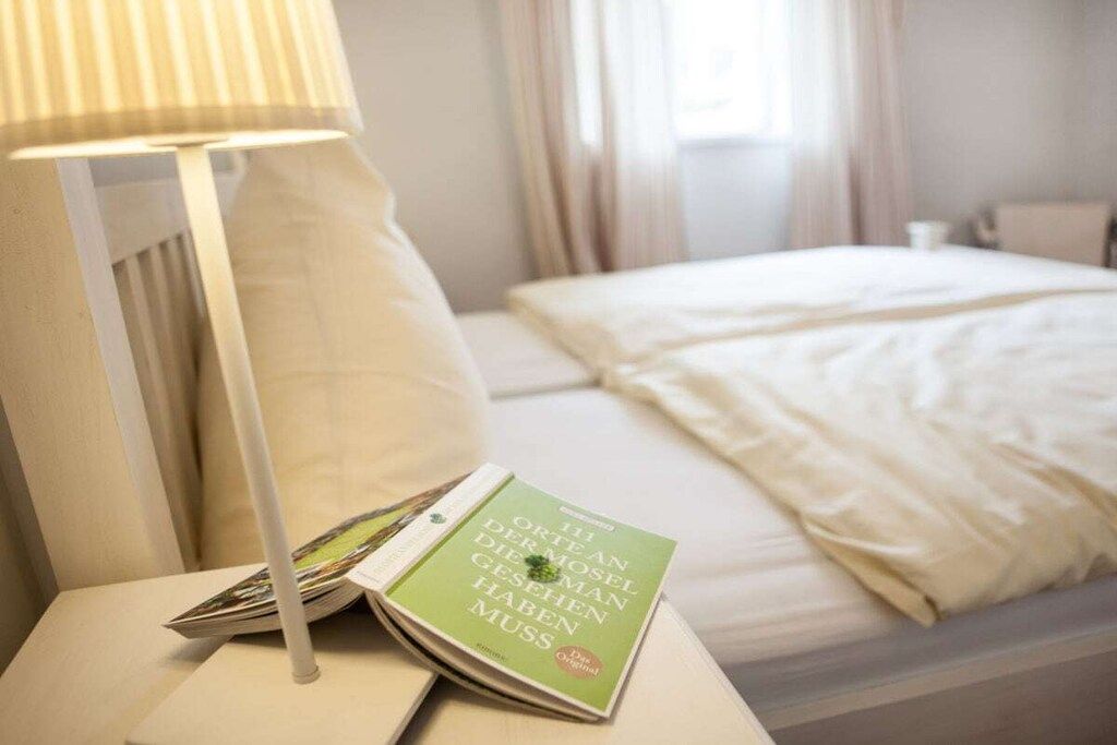 Et hotelværelse med en seng, et natbord, en lampe og en bog.