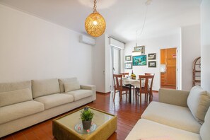 Een woonkamer met een bank, een bijzettafeltje met een plant en een eethoek met stoelen en een tafel.