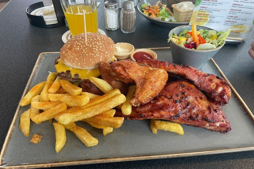 Eine Mahlzeit bestehend aus einem Hamburger, Rippchen und Pommes Frites auf einem Teller.