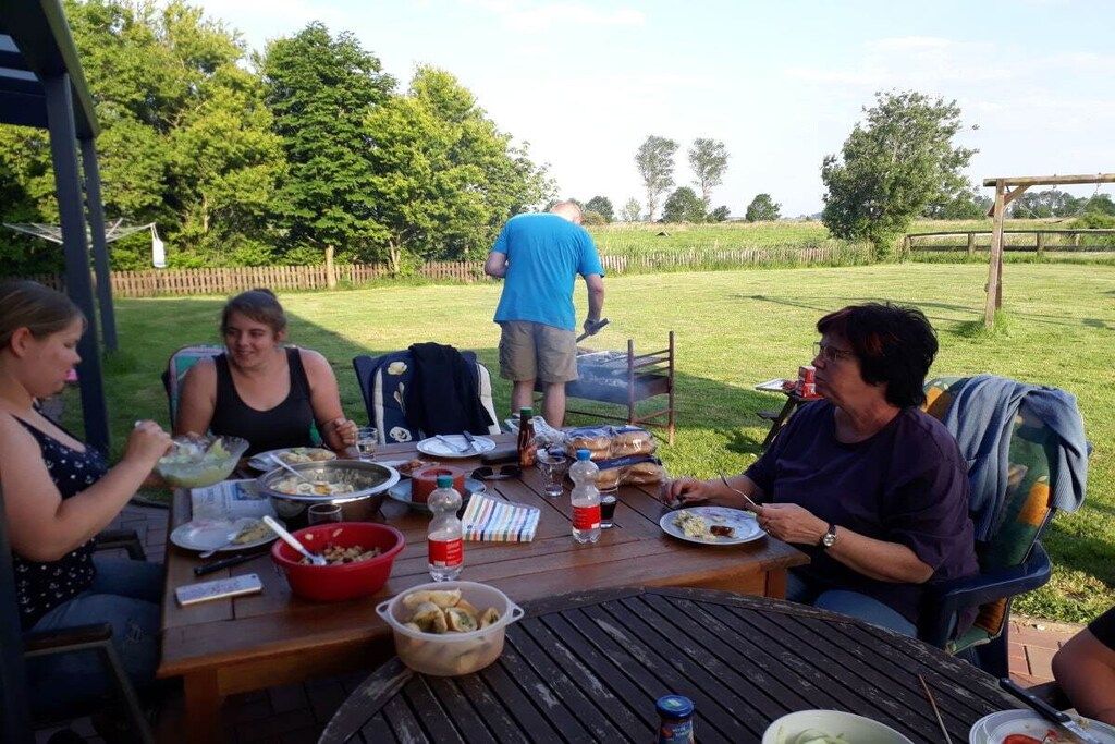 Een buiten eethoek met een ronde tafel, stoelen en een persoon op de achtergrond.