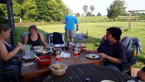 An outdoor dining area with a round table, chairs, and a person standing in the background. - at the Wäcken holiday farm (Krummhörn-Grimersum)