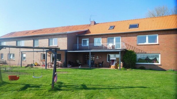 A two-story residential building with a covered patio, a swing set, and a visible window. - at the Wäcken holiday farm (Krummhörn-Grimersum)