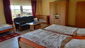 A room with two beds, a sofa, a wooden wardrobe, a small table, and a view of the outdoors. - at the Wäcken holiday farm (Krummhörn-Grimersum)