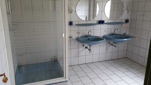 A bathroom with two sinks, two mirrors, and a shower enclosure. - at the Wäcken holiday farm (Krummhörn-Grimersum)
