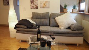 Uma sala de estar moderna com um sofá, uma mesa de centro de vidro, uma garrafa de vinho e um copo de vinho.