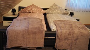 Uma cama de casal com peseira, duas mesas de cabeceira com abajures e uma janela com cortinas leves.