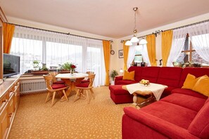 A living room with a red sofa, a dining table with chairs, and a television. - Holiday apartment with 1 bedroom (Grainau)
