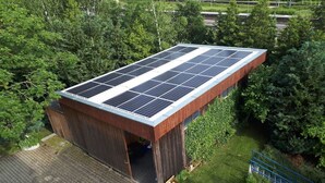 Um edifício com telhado solar, rodeado por vegetação.