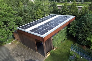Een gebouw met een dak van zonnepanelen, omringd door groen.