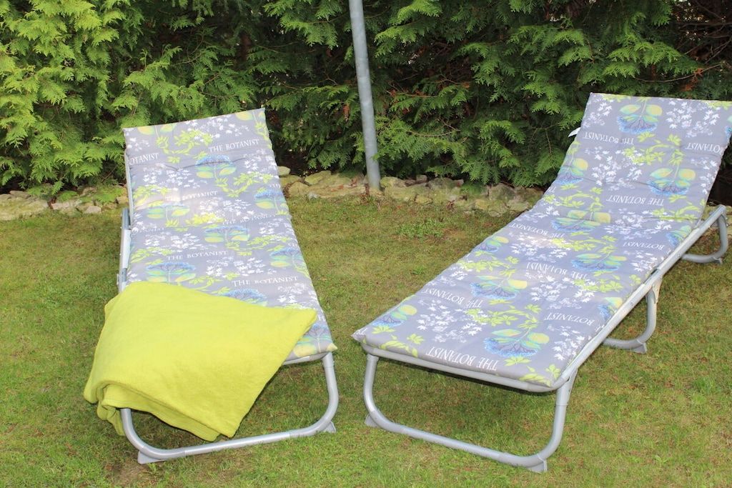 Zwei Gartenlounge-Stühle mit botanischem Muster, einer mit einem gelben Handtuch, vor dem Hintergrund üppiger Pflanzen.