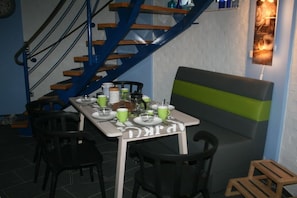 Een eethoek met een tafel gedekt voor vier personen, stoelen, een bank en een trap met houten treden en blauwe leuningen.
