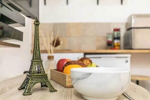 A kitchen with a marble bowl, a model of the Eiffel Tower, and a fruit bowl with apples and oranges. - Charming studio - 2P - Voltaire (Paris)