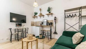 Un espacio habitable compacto con kitchenette, zona de comedor, sofá y televisor montado en la pared.