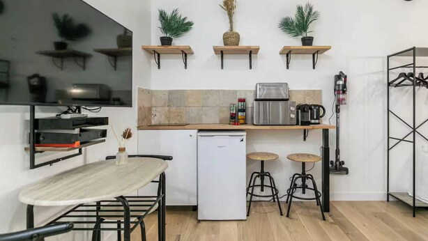 Una cocina compacta con refrigerador, microondas, tostadora y cafetera. Hay tres taburetes y una mesa con sillas.