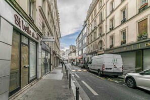 A street with storefronts, a white van, and a parked car. - Charming studio - 2P - Voltaire (Paris)