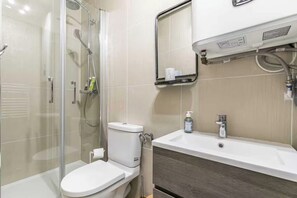 A modern bathroom with a glass-enclosed shower, a white toilet, a sink with a mirror, and a towel rack. - Charming studio - 2P - Voltaire (Paris)