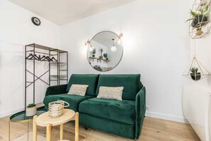 A green sofa with cushions, a round mirror, a coat rack, and a small table with a plant. - Charming studio - 2P - Voltaire (Paris)