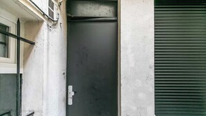 Una puerta cerrada con manija, una ventana a la izquierda y un persiano verde a la derecha.