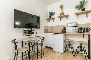 A compact kitchen with a flat-screen TV, a mini-fridge, a coffee maker, and bar stools. - Charming studio - 2P - Voltaire (Paris)