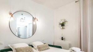 Habitación de hotel con un espejo grande y redondo, dos almohadas, una cama con toallas dobladas con esmero, y dos lámparas fijadas a la pared.