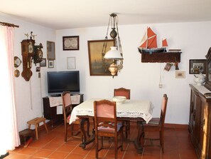 A dining area with a table, chairs, a television, and various wall decorations including clocks and a framed picture. - Holiday Apartment With 1 Bedroom (Krummhoern)