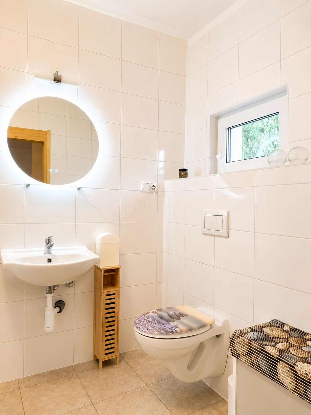 Ein modernes Badezimmer mit einem runden Spiegel, einem Waschbecken, einer Toilette und einem Fenster.