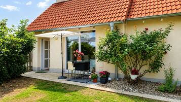 Ein Haus mit rotem Ziegeldach, einer überdachten Terrasse mit Tisch und Stühlen sowie Kübelpflanzen.