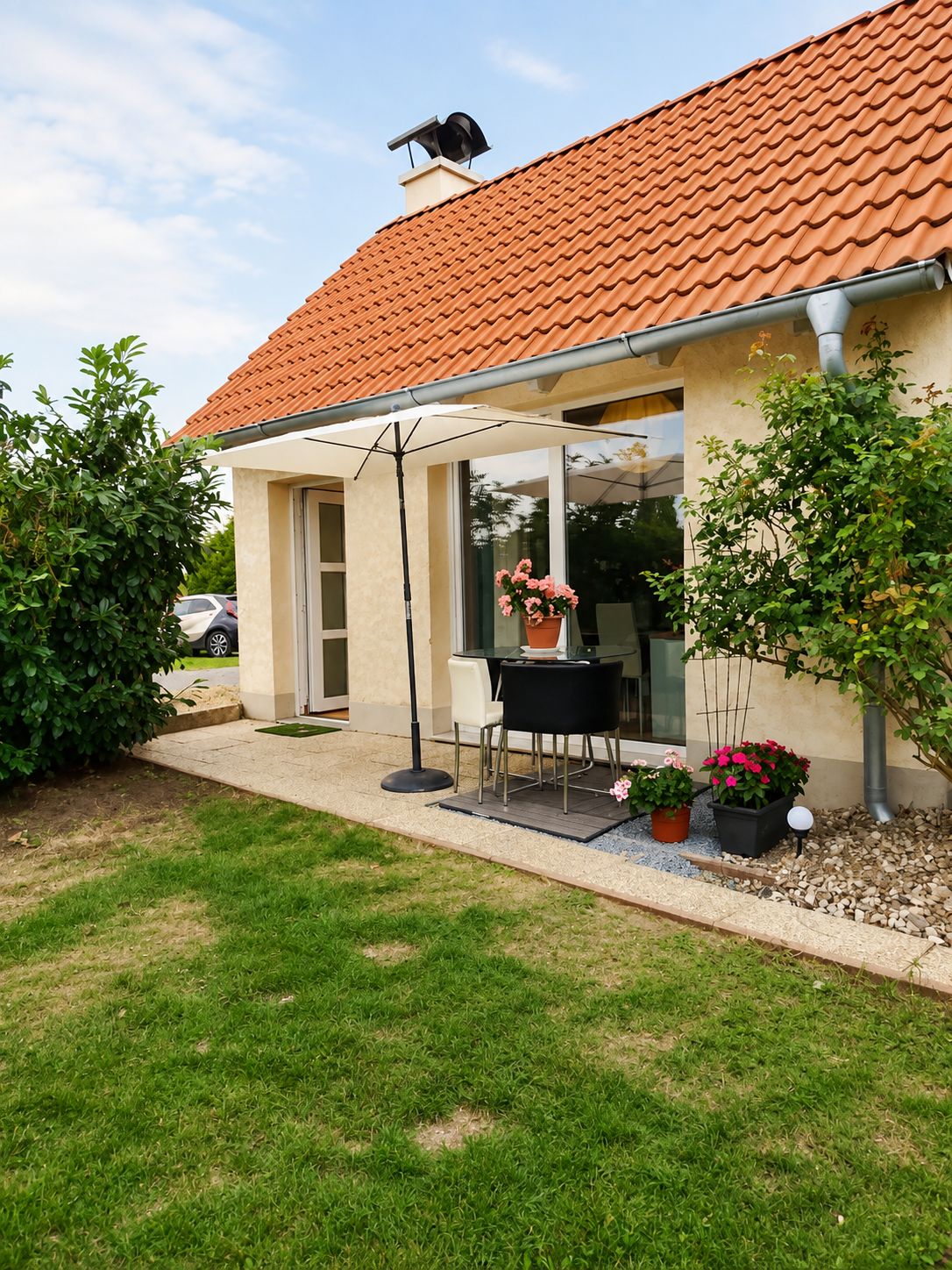 Ein Haus mit Ziegeldach, einer Terrasse mit Tisch und Stühlen und Blumentöpfen.