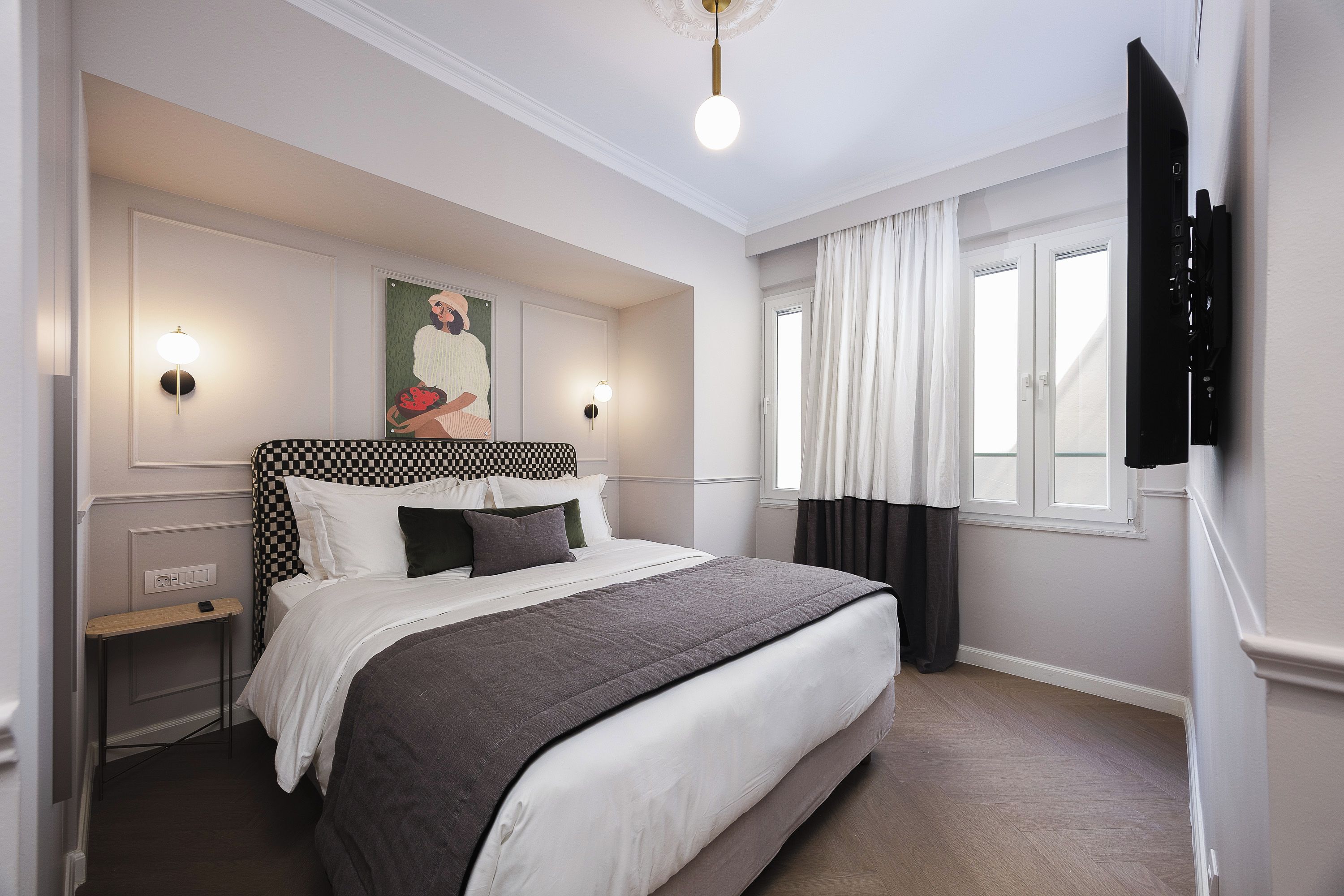 A hotel room with a large bed, two bedside lamps, a flat-screen TV, and a window with curtains.