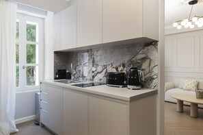 A modern kitchen with a marble backsplash, a built-in coffee station, and a view of the outdoors through a window. - Nouar (Athina)