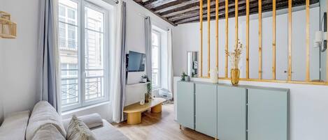 Una sala de estar moderna con un sofá, una televisión, techo de madera y un ventanal grande.
