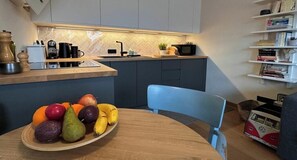 A modern kitchen with a wooden countertop, a bowl of fruit, and a blue chair.