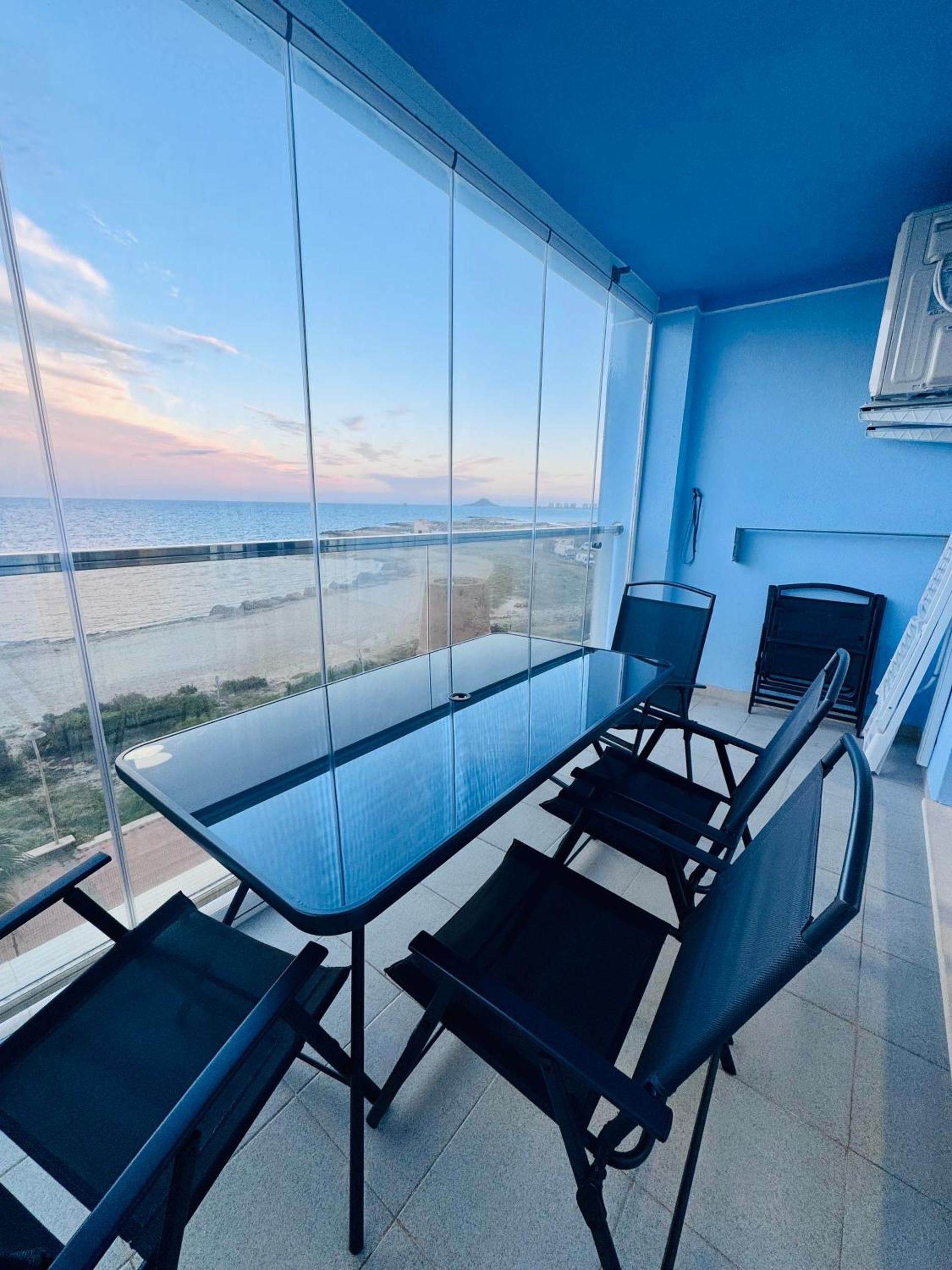 Ein Balkon mit Glastisch und Stühlen, der Blick auf die Küste freigibt.