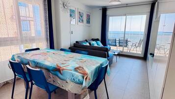Un comedor con una mesa preparada para cuatro personas, un sofá y vistas al mar a través de amplios ventanales.