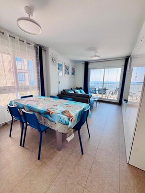 Un coin repas avec une table dressée pour quatre personnes, un canapé et une vue sur la mer grâce à de grandes fenêtres.