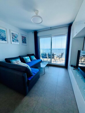 Un salon moderne avec un canapé, une petite table et un balcon offrant une vue sur la mer.