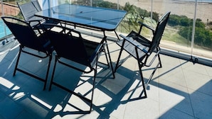 Un balcon avec une table et des chaises en verre, donnant sur une plage et la mer.