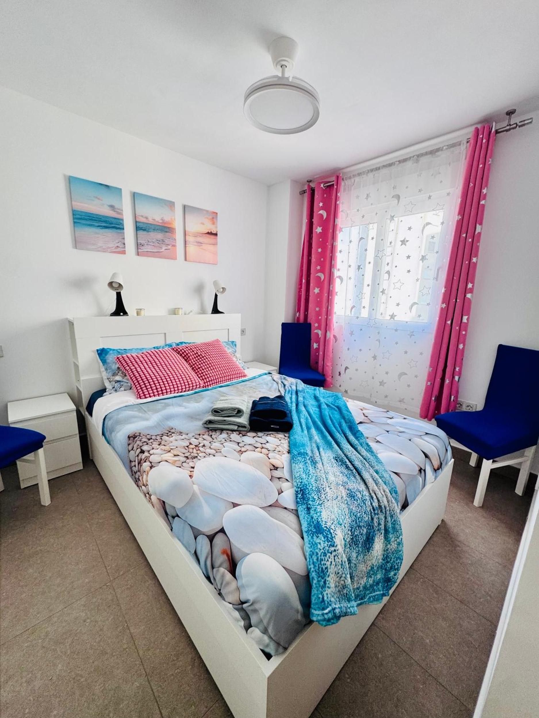 Ein Schlafzimmer mit einem Bett, Nachttischen, einem Deckenventilator und einem Fenster mit Vorhängen.