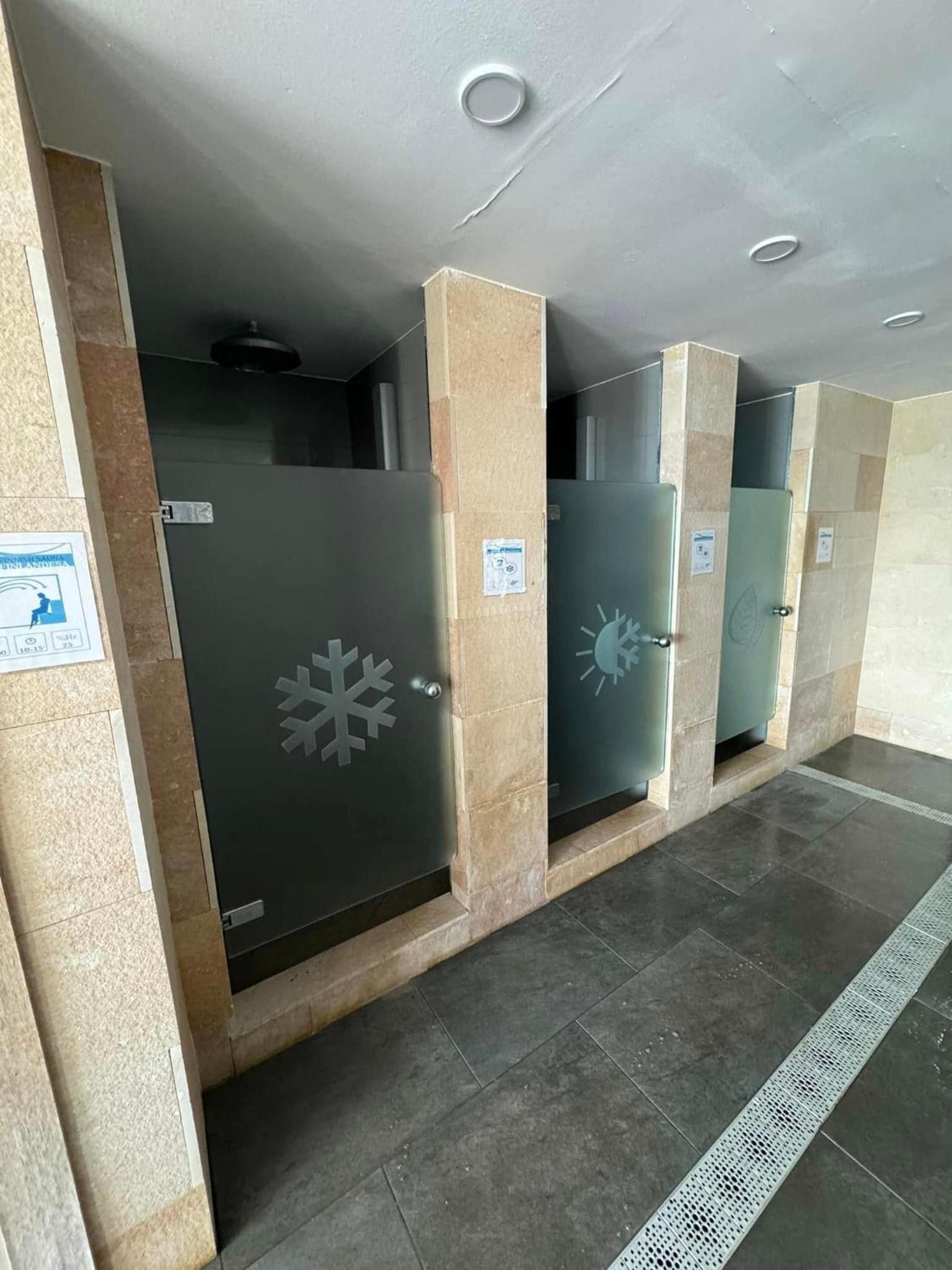 Eine Reihe von dunkelgrauen, metallischen Schließfächern mit Schneeflocken-Designs, vor sandfarbenen Säulen, in einem Flur mit gefliestem Boden und eingelassener Beleuchtung.