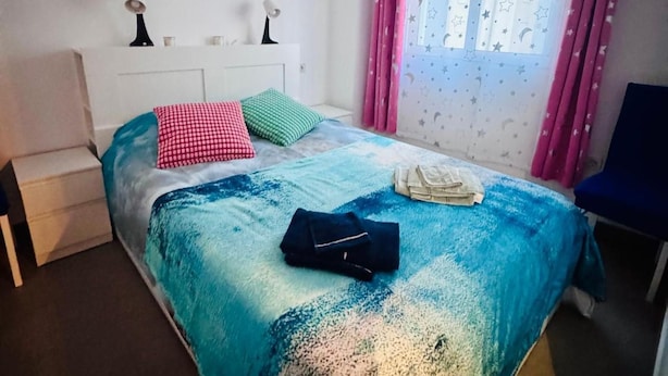 Une chambre à coucher avec un lit, une table de chevet, une chaise et une fenêtre avec des rideaux.