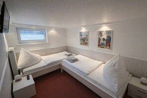 A room with two single beds, a window, a radiator, a small table with a lamp, and two wall-mounted posters. - Holiday apartment with 3 bedrooms (Norderney)